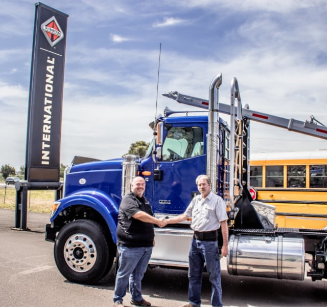 A customer and a salesman shaking hands in front of a brand new international hx series log truck